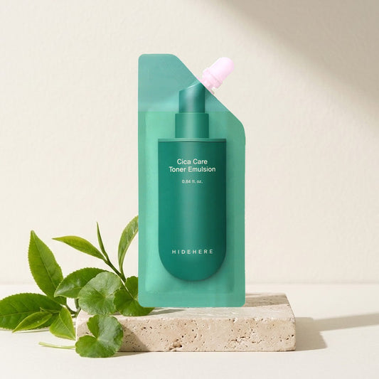 Hidehere Cica Care Toner Emulsion 25 ml sobre una bandeja de travertino, junto a unas hojas verdes