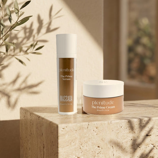 Pack Massada Plenitude: sérum y crema sobre un pedestal de travertino claro, junto a una pared crema con sombras de hojas