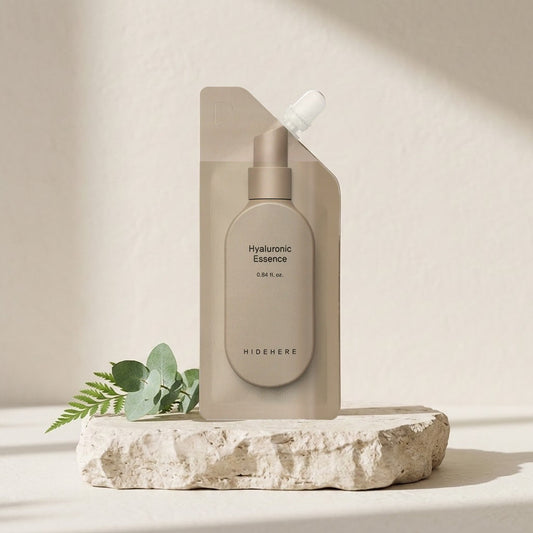 Hidehere Hyaluronic Essence 25ml sobre una losa de piedra rugosa, junto a unas ramitas de hojas verdes
