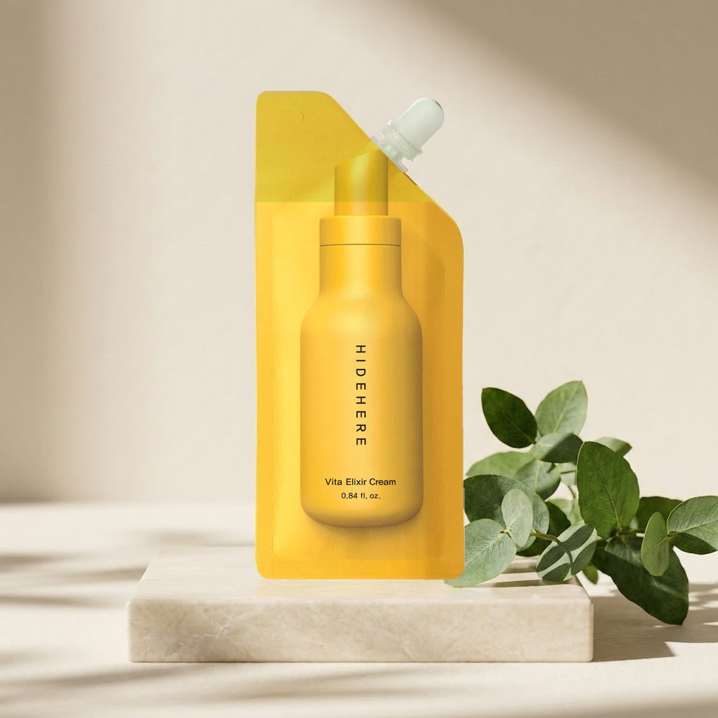 Hidehere Vita Elixir Cream 25 ml sobre una losa de mármol claro, junto a ramas verdes