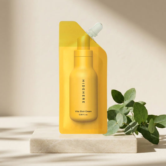 Hidehere Vita Elixir Cream 25 ml sobre una losa de mármol claro, junto a ramas verdes