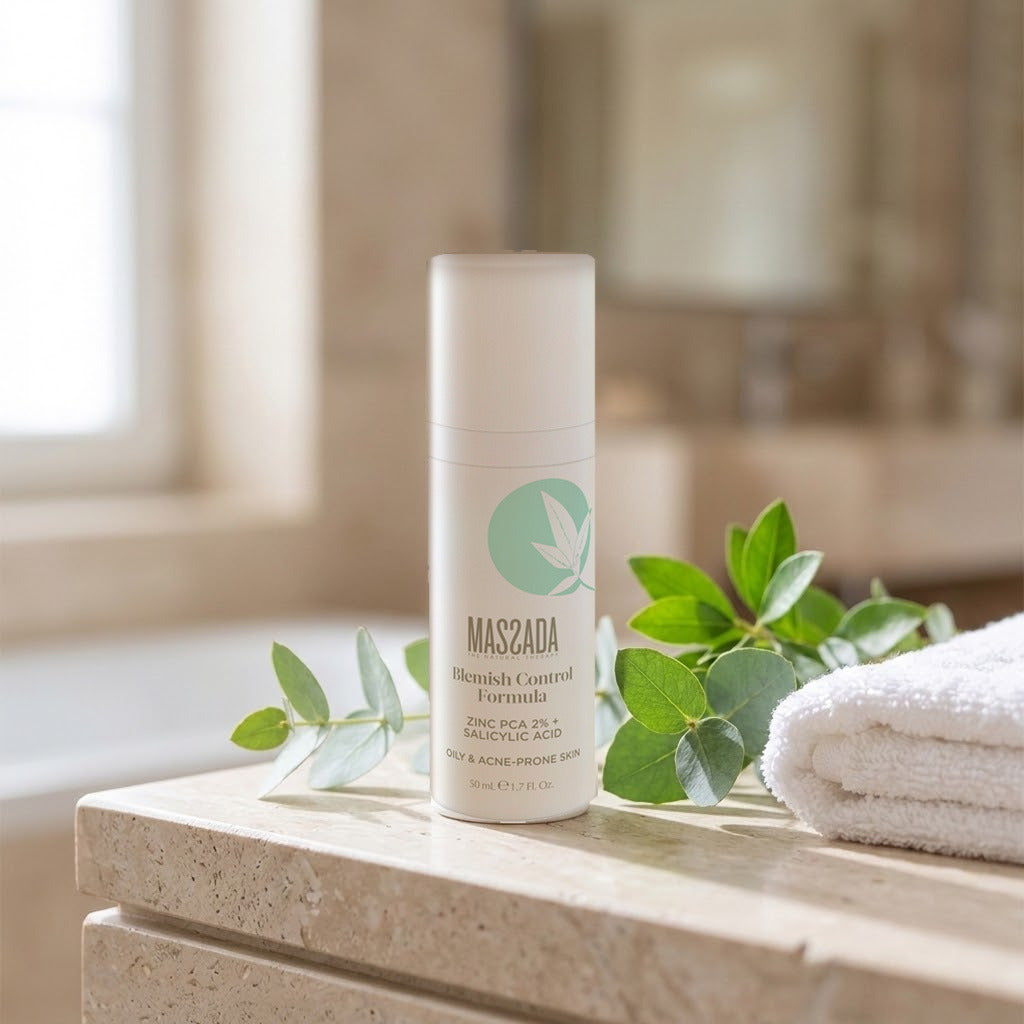 Massada Blemish Control Formula 50 ml sobre una repisa de travertino, junto a ramas verdes y una toalla blanca