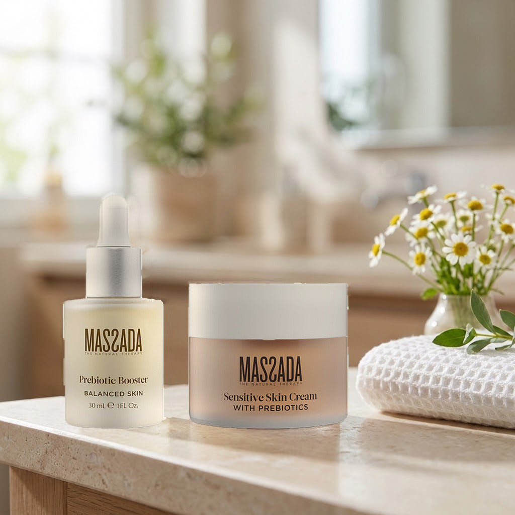 Pack Massada Pieles Sensibles: booster y crema sobre una encimera de piedra clara, junto a flores blancas y una toalla