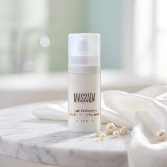 Massada Pearl Perfection Brightening Serum 30 ml sobre una mesa de mármol, junto a perlas y un pañuelo de satén blanco